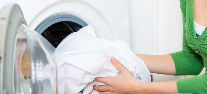 A woman putting white sheets into the washing machine. 