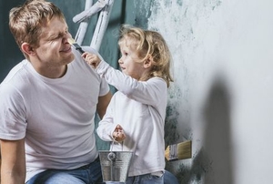 A young girl touches her dad's nose with a paintbrush.
