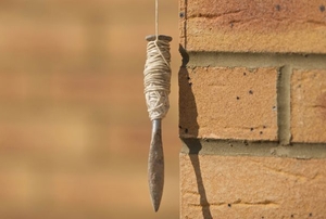 A plumb bob hanging next to a brick wall.