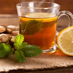 Hot cup of tea next to lemon slice, mint leaf, and ginger root