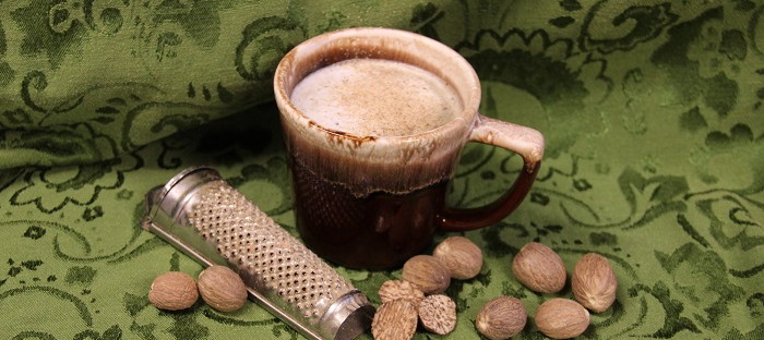 nutmeg grater, nutmeg nuts and cup of coffee with nutmeg sprinkles