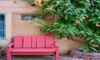 A red bench on a patio in the southwest surrounded by a green vine and a potted herbs.