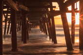sun setting on an ocean under a wooden pier