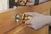 A pair of hands installing a doorknob on a door. 