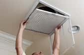 A man replacing an hvac air filter in a ceiling vent. 