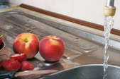 A kitchen sink with peaches and running water.