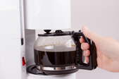 A person pulling a full pot of coffee from the coffeemaker.