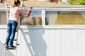 A woman standing on a ladder painting garage door trim.
