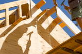 A DIYer framing a house with his shadow cast on the plywood.