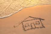 A house drawn in the sand with ocean water washing up toward it. 
