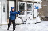 A man shoveling snow outside a house. 