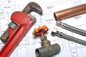 A copper pipe, wrench, valve, and bolts sit on top of construction plans.