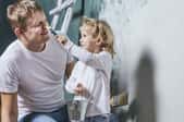 A young girl touches her dad's nose with a paintbrush.