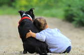 Child leaning on a black dog with a red collar
