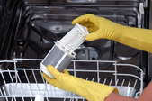 Someone wearing yellow rubber gloves removing and cleaning a dishwasher filter.