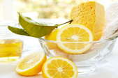 Natural and organic cleaning products in glass bowl with lemon, dish sponge, cleaning cloth, and natural liquid soap.