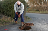 A man using a drain snake in a hole in the street