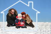 A family sits outside on the snow surrounded by the outline of a house.