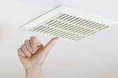 Person reaching towards an exhaust fan in the ceiling.