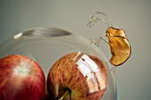 A bug made of an apple slice, sitting on a glass container filled with apples. 