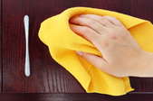 a hand cleaning a dark kitchen cupboard with a yellow cloth