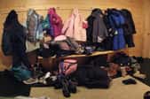 A messy, cluttered mudroom, filled with shoes, bags, and jackets.