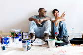 two smiling people in an apartment room with painting supplies looking at the walls