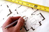 a hand drawing blueprints and a yellow tape measure crossing the blueprint