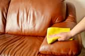A homeowner cleaning spills from their faux leather sofa using a soft yellow cloth.