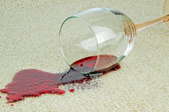 A wine glass knocked over on a carpet with spilled red wine.