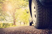A close-up image of a car tire on asphalt with sun shining down. 
