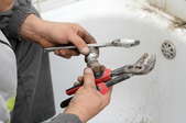 A plumber holding a wrench trying to fix a leaky drain.
