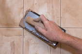 Spreading grout between tiles by hand, leaving some behind.