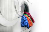 A rainbow selection of shirt hanging over the edge of a white washing machine basin.