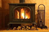 A fire roaring in a wood burning stove with firewood underneath it.
