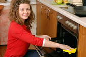 A woman cleaning the inside of her oven with a rag.