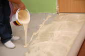 Carpet glue being poured on a concrete floor.