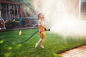 A girl holding a hose that's spraying water all over a lawn in a backyard.