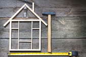 A small house made of sticks next to a hammer and a tape measure.