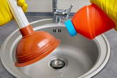 gloved hands with plunger and liquid above small metal sink
