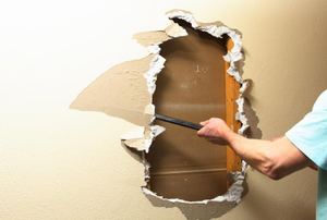 hand using crowbar on hole in sheetrock
