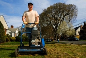 A man pushing gas powered rake, dethatching his front yard.
