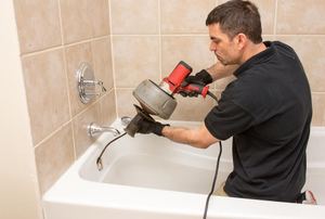 A man uses a plumber snake.