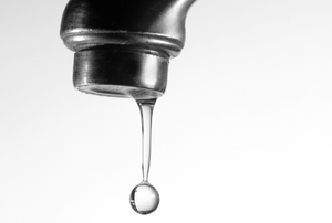 A large water drop falls from a leaking faucet.