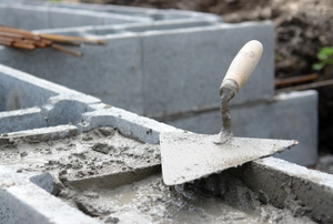 A trowel resting on top of a cinder block wall with mortar. 