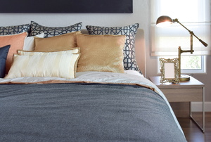 Bedroom with grey duvet, throw pillows, and sleek nightstand.