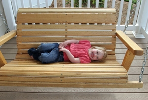 A smiling female toddler laying sideways on a wooden porch swing.