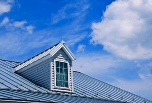 A window jutting out of a metal roof against a partly-cloudy sky.