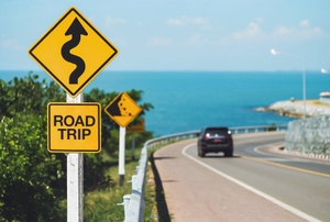 A car drives on a windy road near the ocean.