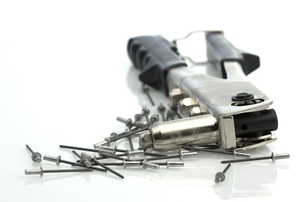 A pile of pop rivets next to a pop rivet gun.